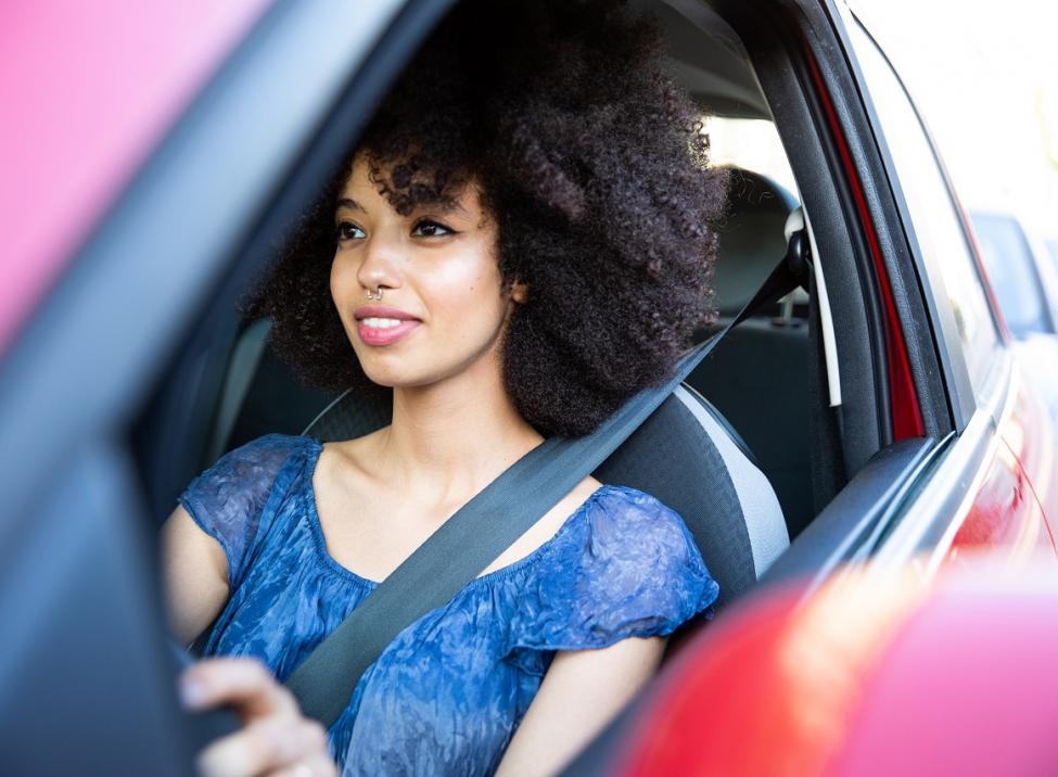 Mujer sonriendo mientras conduce un auto rojo