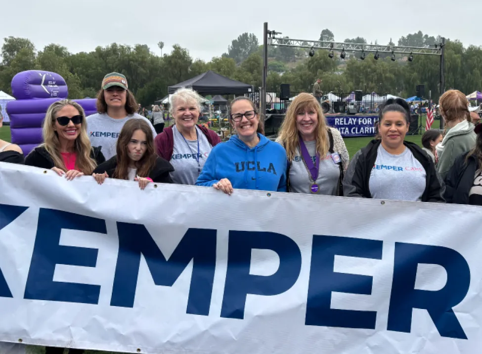 Los voluntarios de Kemper Cares sostienen una pancarta de Kemper mientras participan en un evento al aire libre
