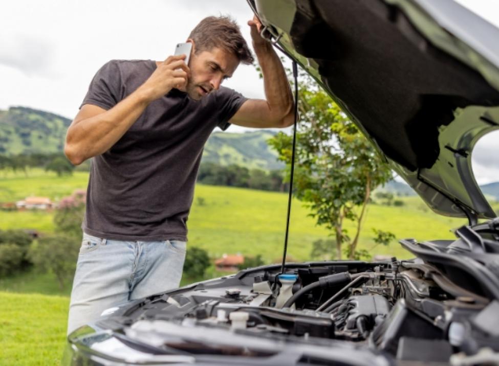 Cliente en el teléfono observando el compartimiento del motor debajo del capó del auto