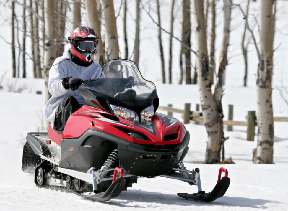 Photo of a person riding a red snowmobile with a red helmet