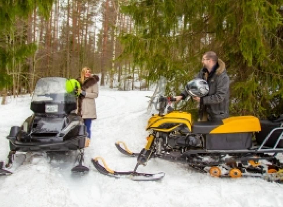 Two people who are taking a break from snowmobiling chat beside their sleds.